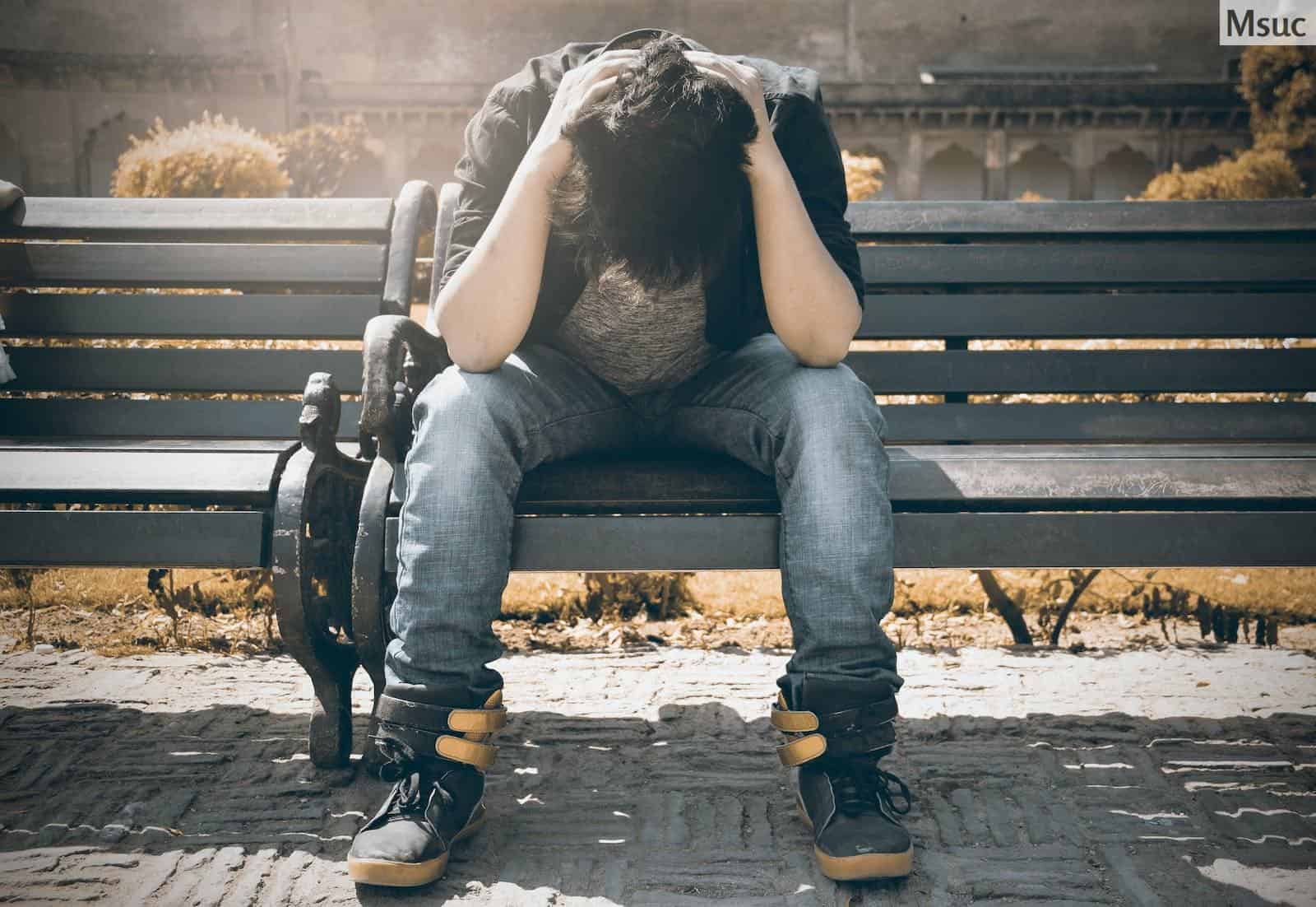 Man in Black Shirt and Gray Denim Pants Sitting on Gray Padded Bench