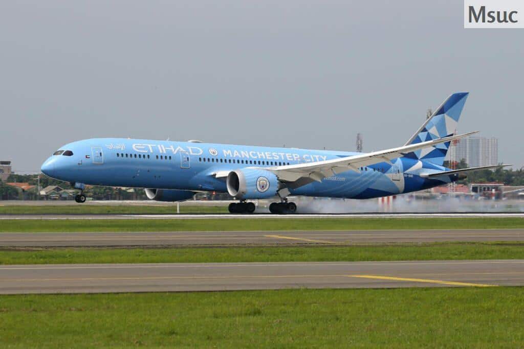 Etihad Airways airplane featuring Manchester City livery landing on runway.