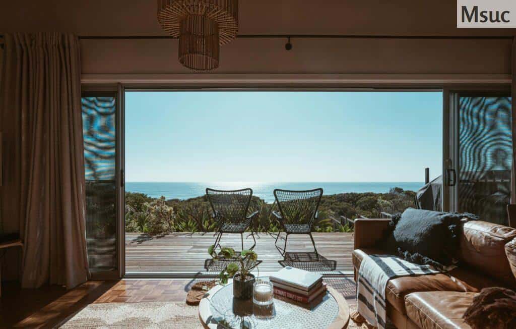 Interior design of luxurious apartment with large balcony doors and wooden terrace having picturesque view on green forested seashore and calm blue sea