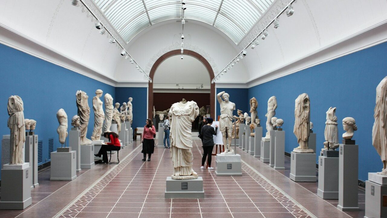 Sala de museo con esculturas clásicas y visitantes recorriendo la galería