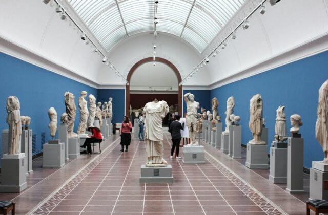 Sala de museo con esculturas clásicas y visitantes recorriendo la galería