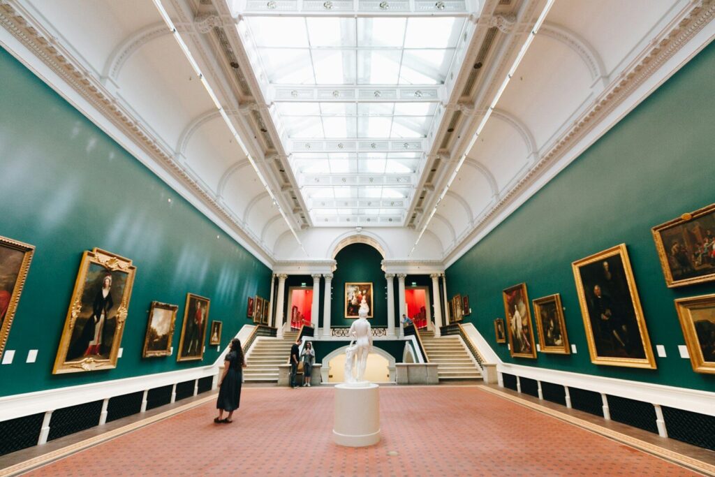 Galería de pintura con paredes verdes y una escultura al fondo